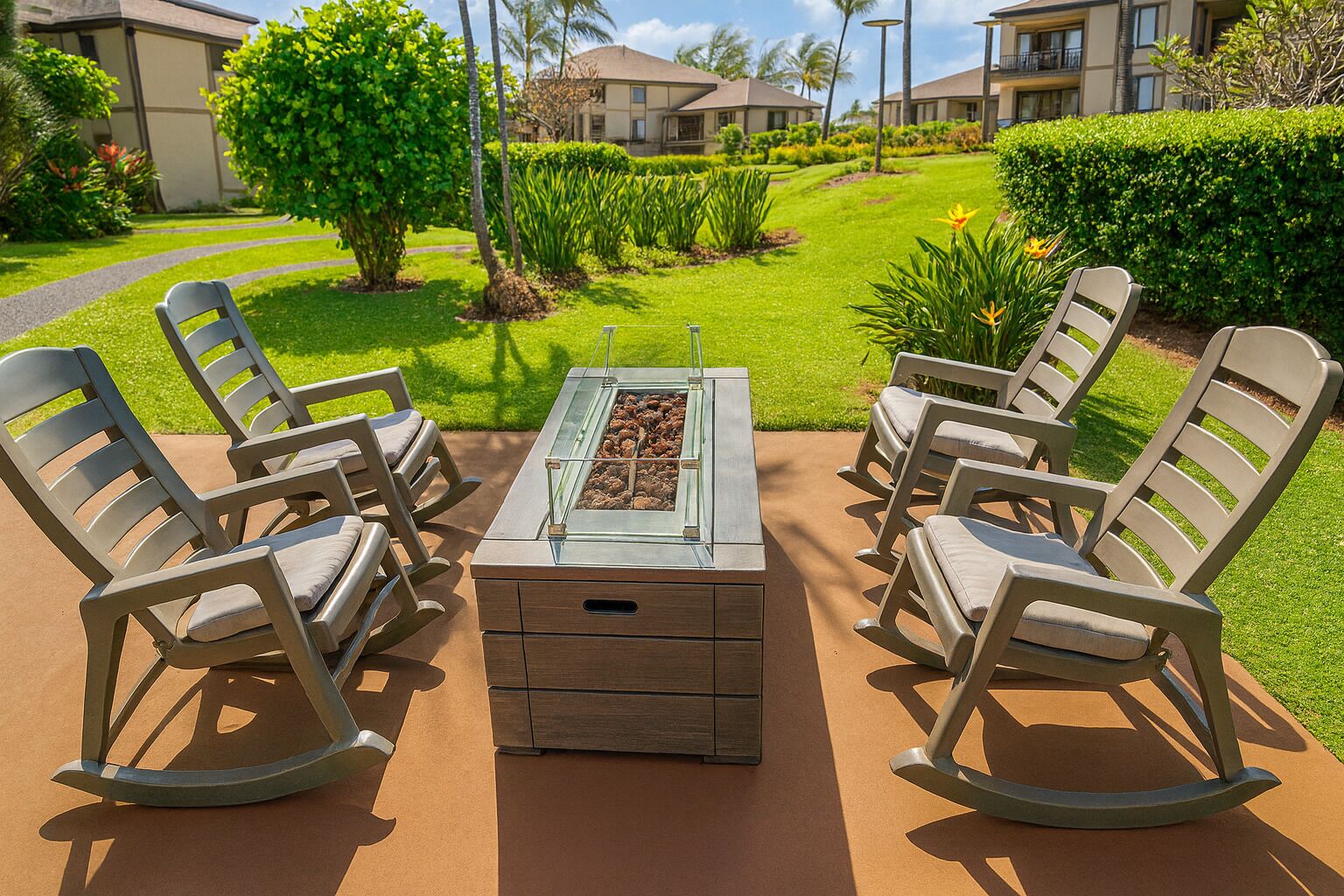 Eine Terrasse mit vier Schaukelstühlen und einem Tisch mit Glasplatte, umgeben von gepflegter Bepflanzung und Blick auf eine Wohngegend.
