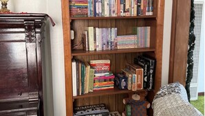A bookshelf filled with books and board games, a lamp, and a stuffed toy on a wooden floor.
