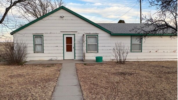 A single-story house with a green roof and white siding, a front door, and two windows.