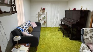 A living room with a dark-colored sofa, a green carpet, a piano, and a television.
