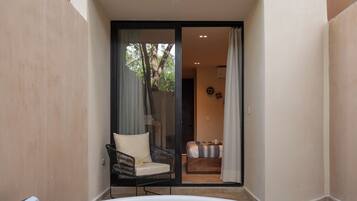 Un jacuzzi en un patio con una silla y un sofá, una puerta corrediza de vidrio que da a una habitación y una pared color beige.