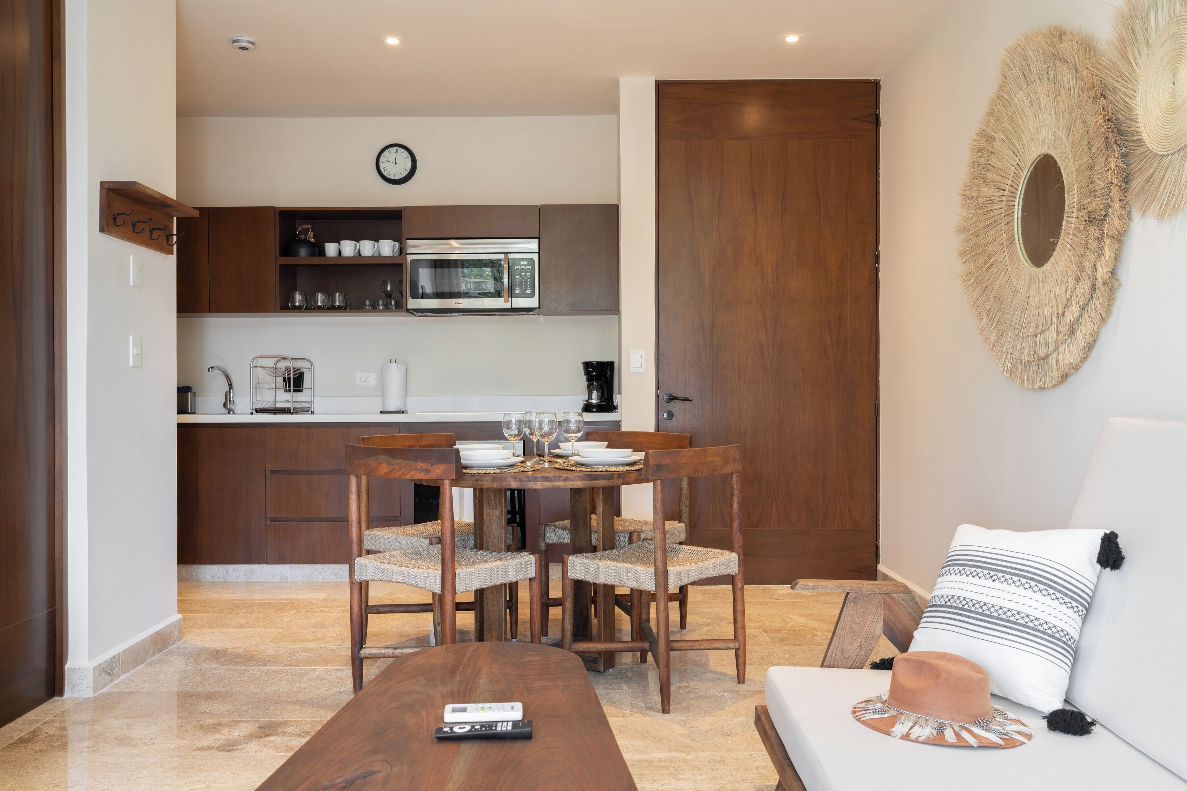 A modern kitchen with a dining area, a sofa, and a remote control on a wooden table.