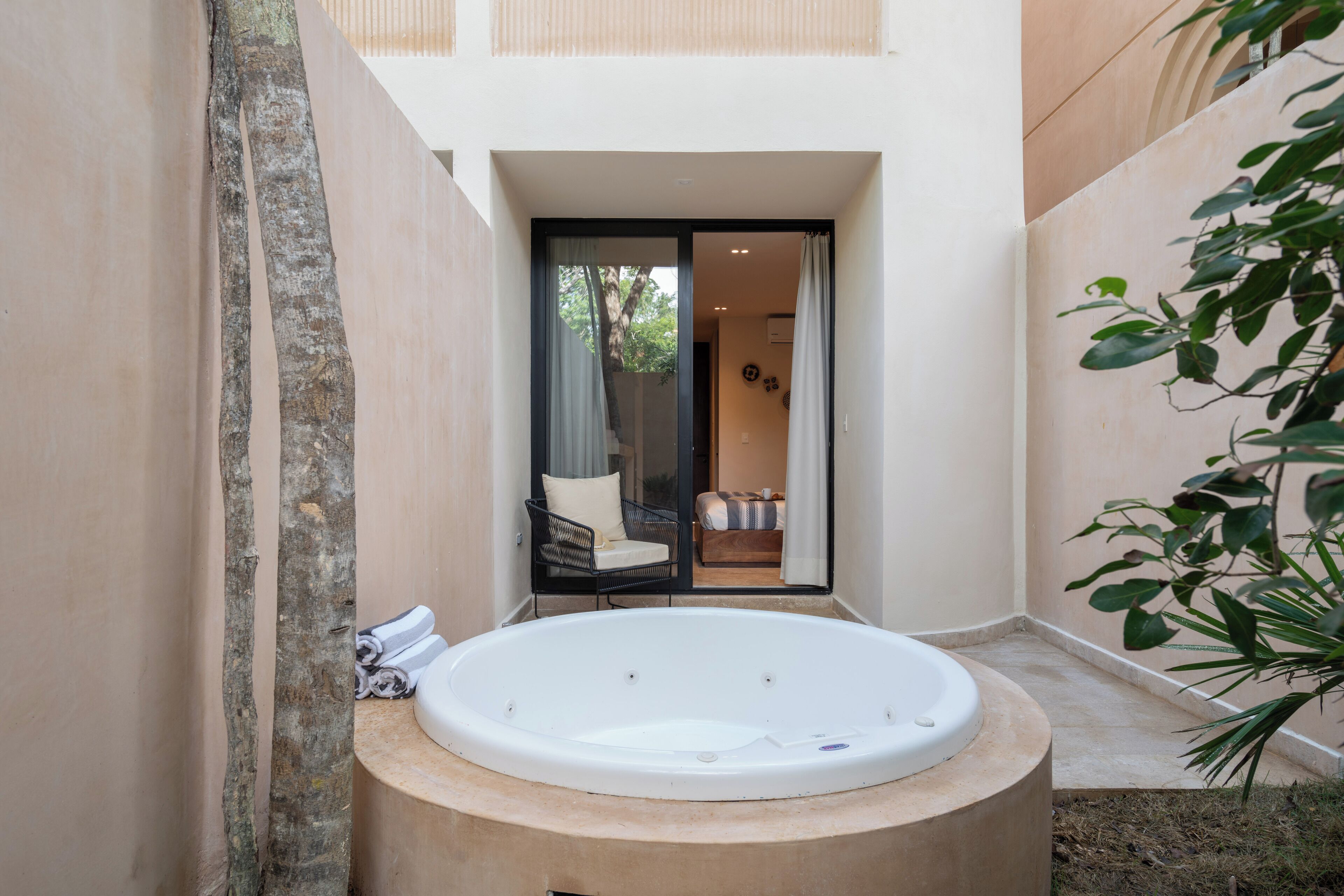 A spa area with a hot tub, a chair, and a view of a balcony with a sofa and curtains.