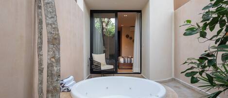A spa area with a hot tub, a chair, and a view of a balcony with a sofa and curtains.