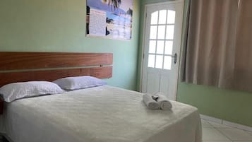 Una cama bien hecha con sábanas blancas y toallas enrolladas, cabecera de madera, una puerta con ventana y un cartel en la pared.