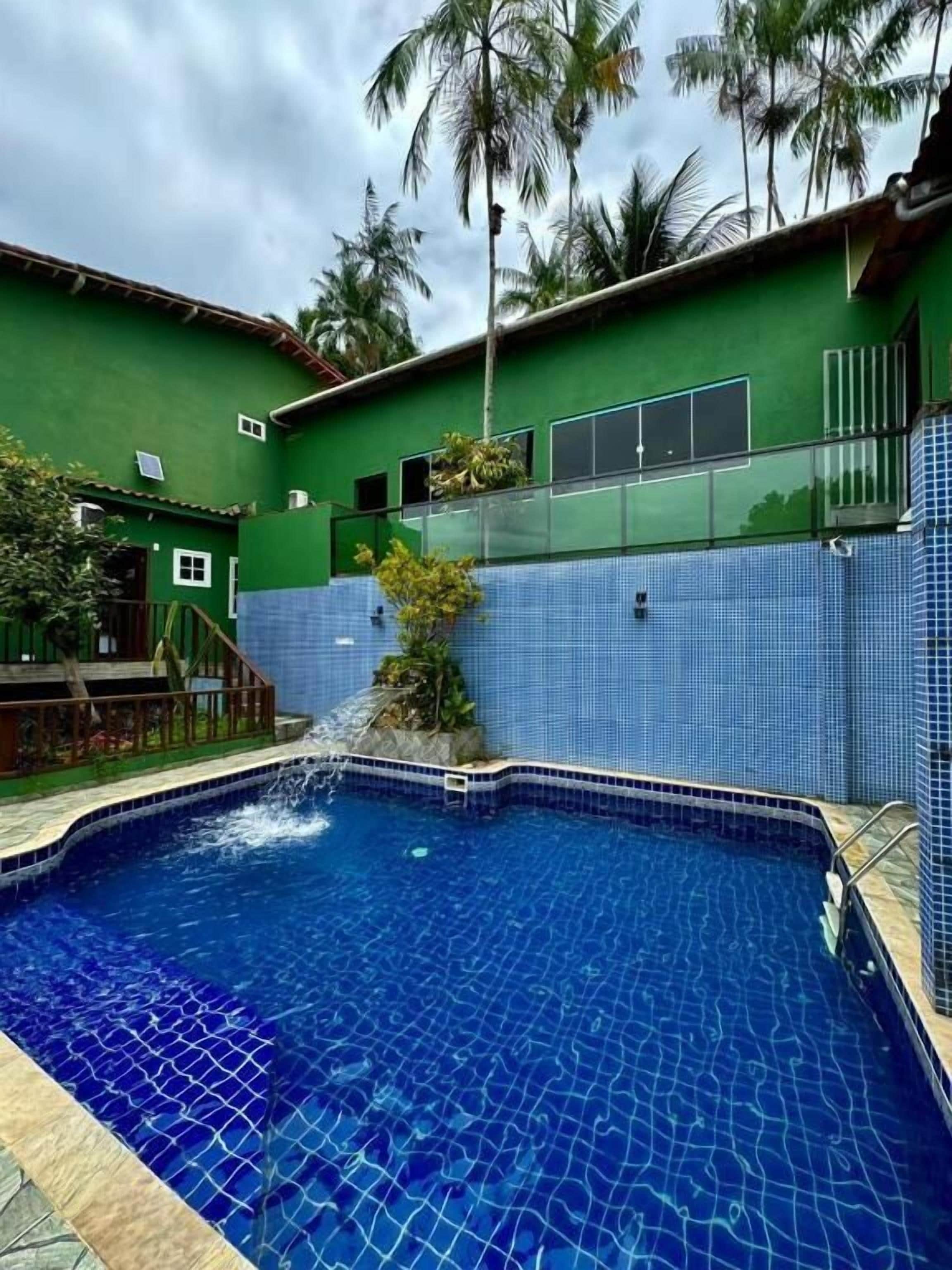 A swimming pool with clear blue water, surrounded by a green building with a tiled wall and a small waterfall feature.