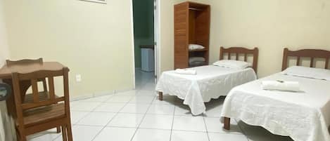 A bedroom with two beds, a wooden wardrobe, a desk, and a chair.