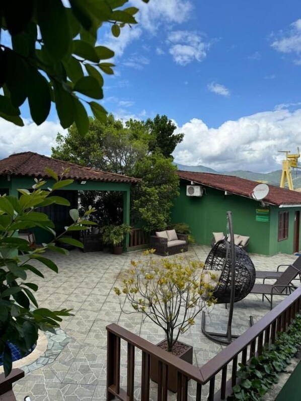A courtyard with a green building, outdoor seating, and a satellite dish. - Pousada Platôdasilhas (Angra dos Reis)