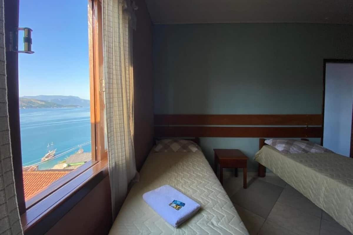 Une chambre avec deux lits, une petite table et une fenêtre donnant sur la mer.