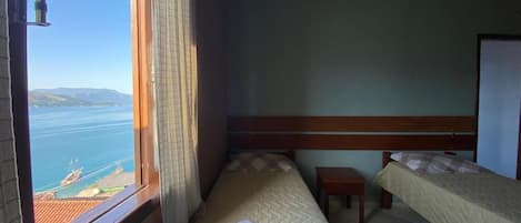 Ein Zimmer mit zwei Betten, einem kleinen Tisch und einem Fenster mit Meerblick.