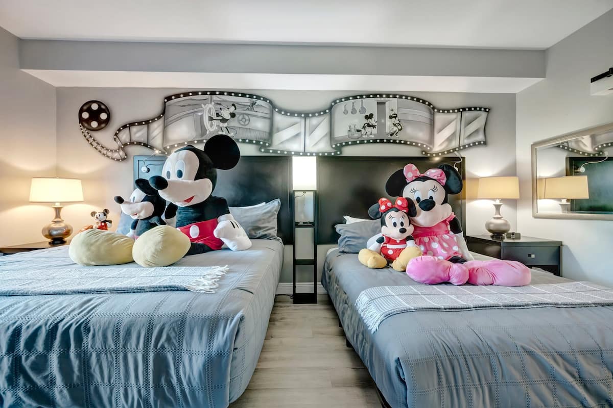 A hotel room with two beds, a large mirror, and a wall mural featuring Mickey and Minnie Mouse.