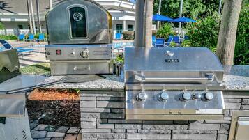 Une cuisine extérieure dotée d’un barbecue intégré et d’un fumoir, le tout installé devant un mur en pierre.