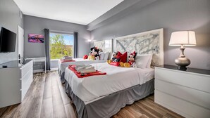Quarto de hotel com cama, escrivaninha, televisão e janela com cortinas.