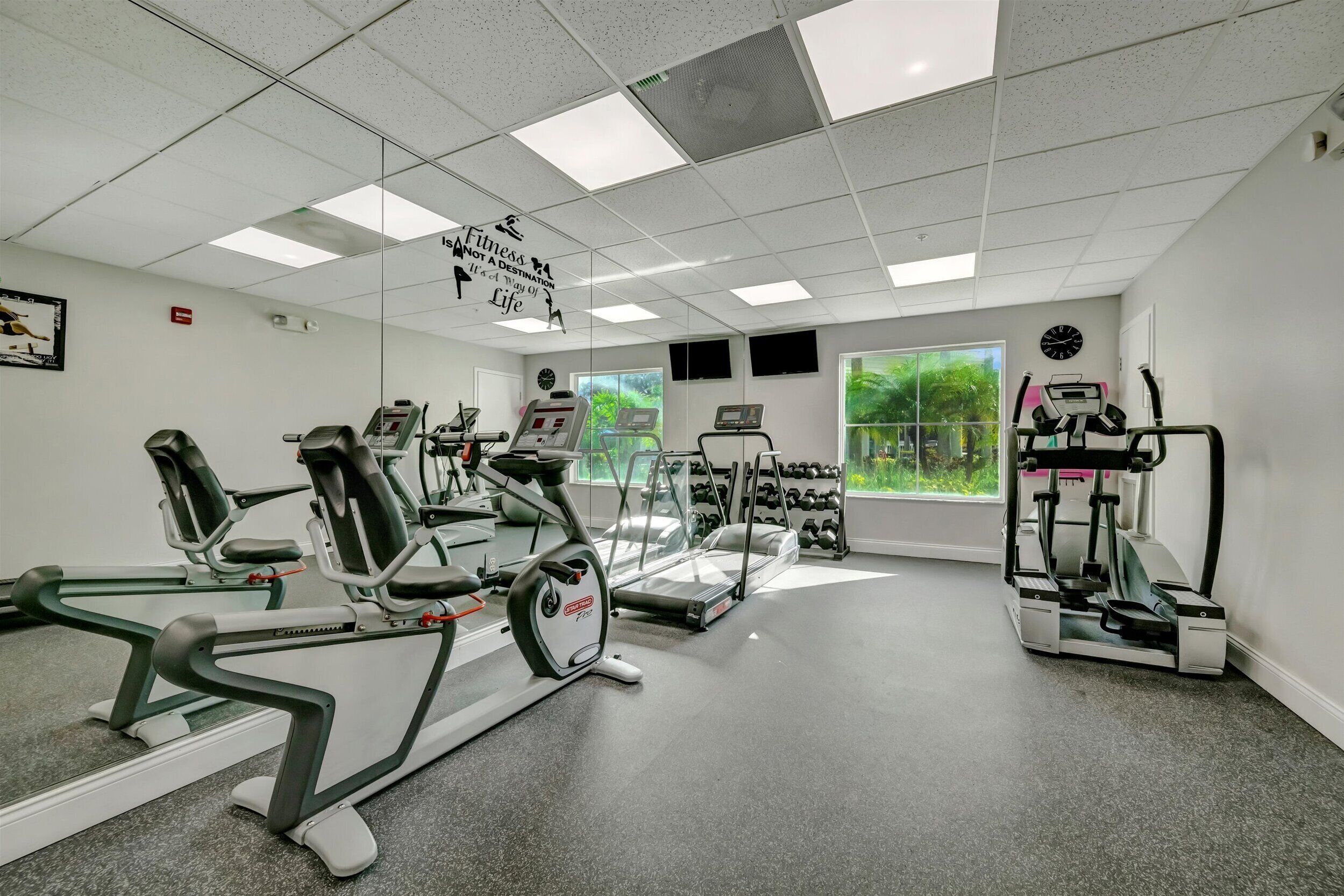 Une salle de sport équipée de divers appareils d’exercice, notamment des tapis de course et des vélos d’appartement, et dotée d’un grand miroir sur l’un des murs.