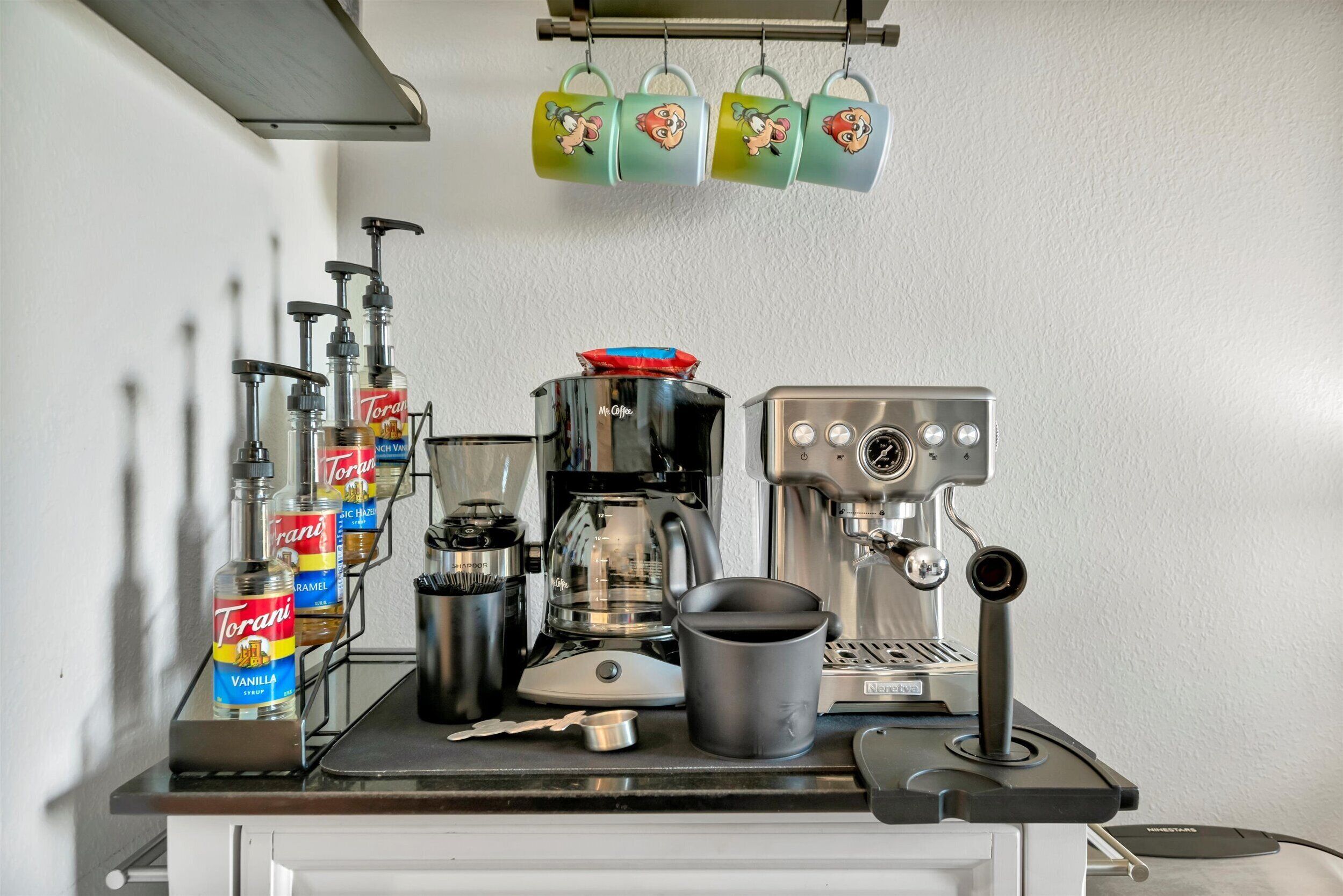 Eine Kaffeemaschine zusammen mit Torani-Sirupflaschen, einer Kaffeemühle und einem Wasserkocher auf einer Küchenarbeitsplatte.