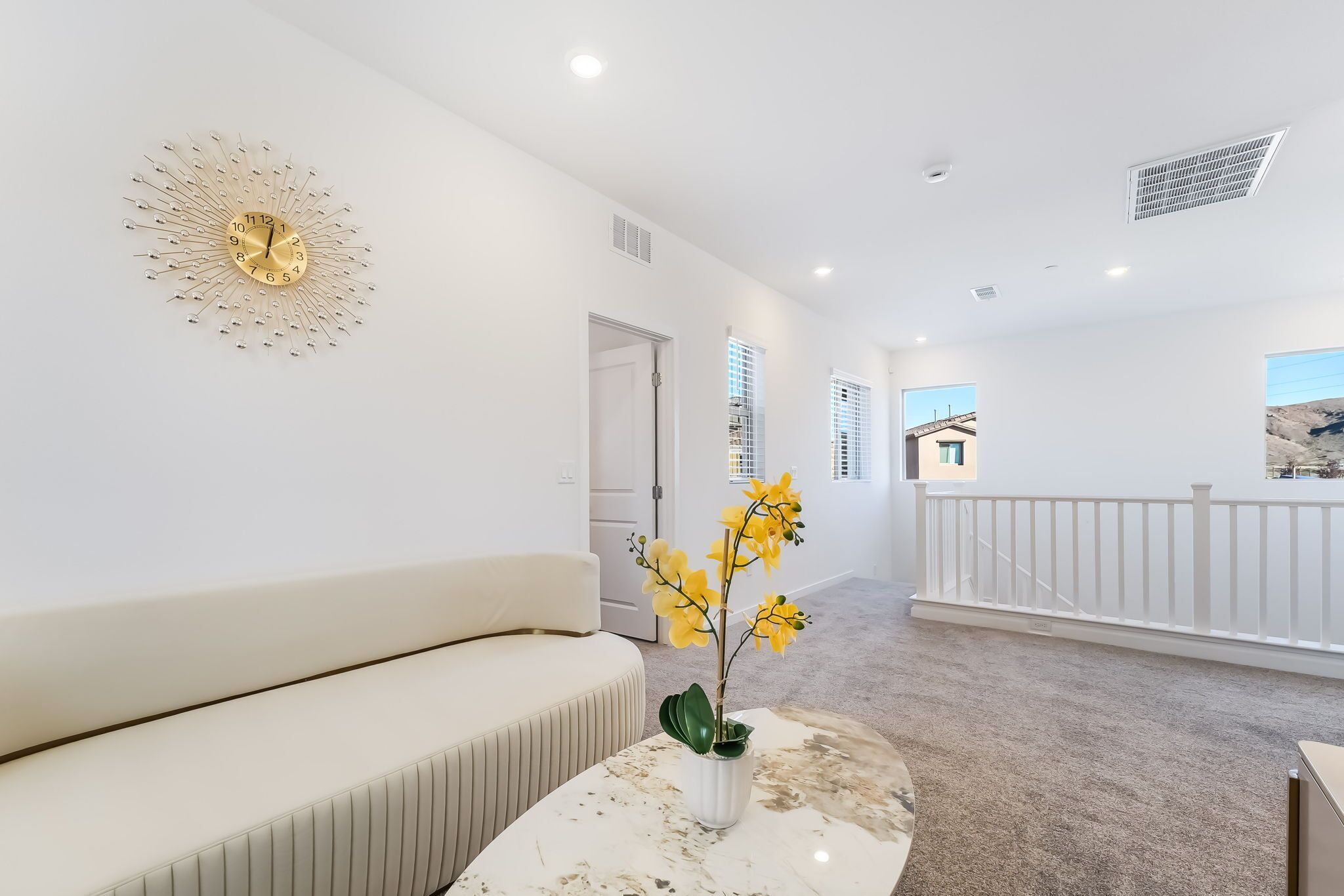 Een modern interieur met een witte bank, een marmeren tafel met een vaas met gele bloemen, en een bijzondere wandklok.