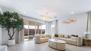 A modern living room with a large potted tree, a beige sofa set, and a round coffee table. - Resort-Style 4BR Home in Lake Las Vegas-Near Strip (Henderson)