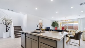 A modern kitchen with a central island, a dining area with a sofa and chairs, and a staircase leading to an upper level. - Resort-Style 4BR Home in Lake Las Vegas-Near Strip (Henderson)