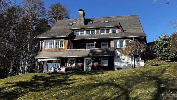 Een woonhuis met twee verdiepingen, een schuin dak, meerdere ramen en een veranda.