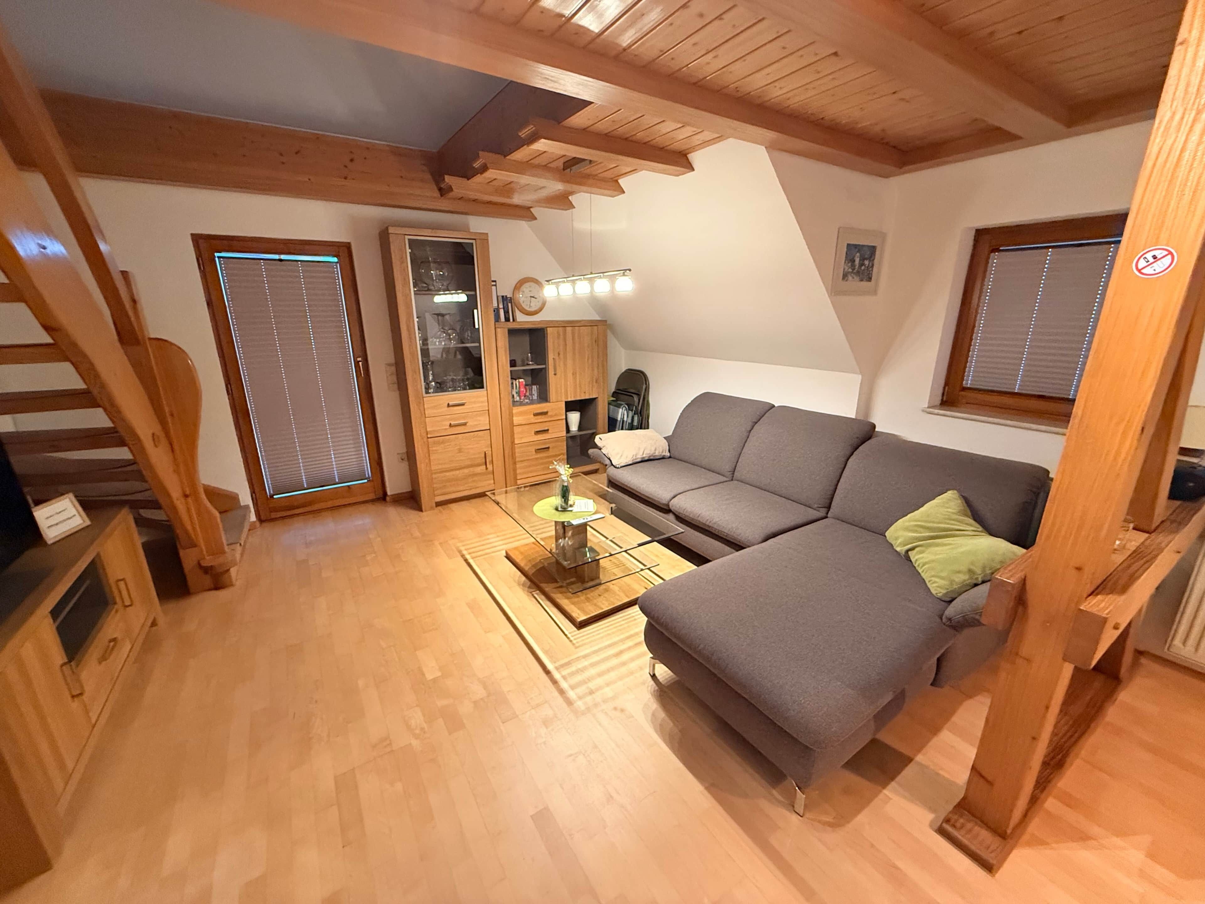 Ein gemütlicher Loft-Raum mit einer Holztreppe, einem grauen Sofa, einem Glastisch und einem Holzschrank.