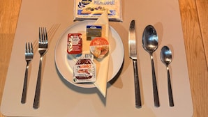 Twee eettafels met borden, bestek en verpakte etenswaren op placemats.