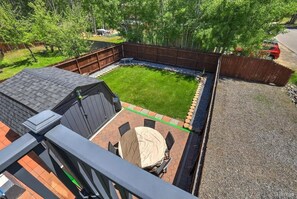 Ein Garten mit überdachter Terrasse, einem eingezäunten Bereich und einem Geräteschuppen.