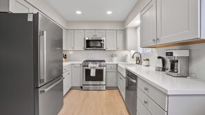 Una cocina moderna con electrodomésticos de acero inoxidable, armarios blancos y encimera de madera.