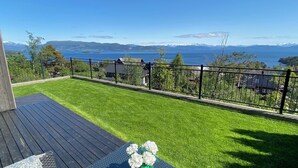 A deck with a table and chairs, a grassy lawn, and a view of a lake and mountains. - Beautiful ocean and fjord view short distance to Bergen (Vestland)