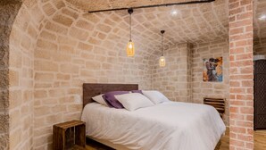A bedroom with a stone wall, a wooden floor, a bed with white bedding, and two hanging light fixtures. - Romantic accommodation for two with Moonlove duo whirlpool bath (Vence)