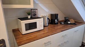 Cozinha compacta com micro-ondas branco, cafeteira e chaleira sobre bancada de madeira.