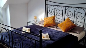 Uma cama com estrutura de metal, um cobertor azul e dois travesseiros amarelos.