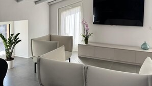 A modern living room with a high ceiling, a flat-screen TV mounted on the wall, and a minimalist design. - B&B Dimora delle Province (Catania)