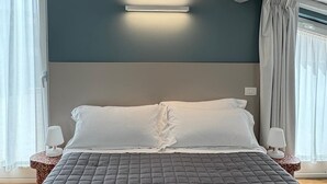 A bedroom with a bed, a bedside table, a wall-mounted light, and a window with curtains. - B&B Dimora delle Province (Catania)