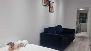 A bedroom with a bed, a dark blue sofa, and a small kitchenette in the background. - Brand New Studio Apartment (Barking)
