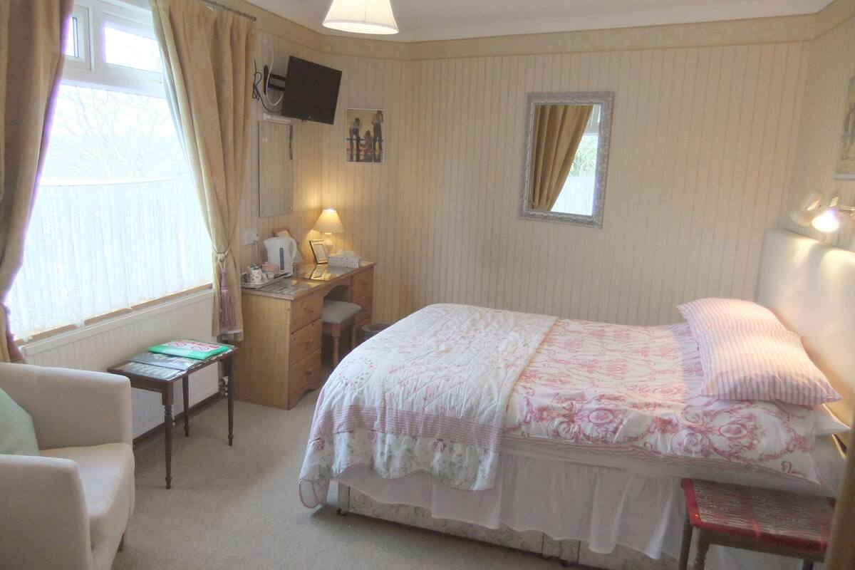 A bedroom with a bed, a desk, a chair, and a window with curtains.