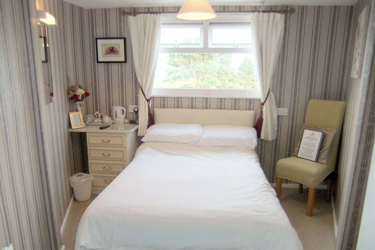 A neatly arranged bedroom with a bed, bedside table, chair, and a window with curtains.