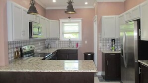 A modern kitchen with white cabinets, granite countertops, stainless steel appliances, and pendant lighting. - Enjoyable 4-bedroom house with AC in charming Highland Park (Highland Park)
