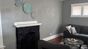 A living room with a fireplace, a gray sofa, and decorative wall art. - Enjoyable 4-bedroom house with AC in charming Highland Park (Highland Park)