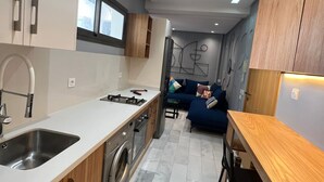 Une cuisine moderne équipée d’un lave-linge intégré, un coin repas avec une table en bois et, au fond, un canapé bleu.