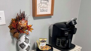 A coffee station with a Keurig machine, a coffee bag, a decorative vase with autumn leaves, and a framed sign saying "Coffee and friends make the perfect blend." - Historic Deereville Home Pet Friendly! (Dubuque)
