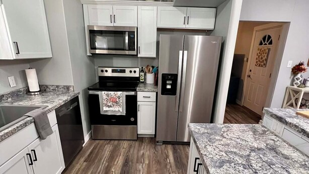 A modern kitchen with white cabinets, a stainless steel refrigerator, an oven, and a microwave. - Historic Deereville Home Pet Friendly! (Dubuque)