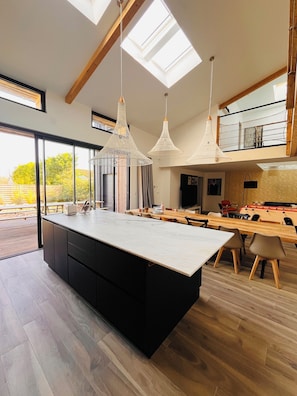 A modern kitchen with a central island, pendant lighting, and a view of the outdoors. - Beautiful renovated farmhouse with swimming pool 5 minutes from Futuroscope (Chasseneuil-du-Poitou)