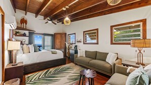 Un dormitorio con cama, sofá, mesa de centro, lámpara, ventilador de techo y ventana con vistas.