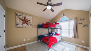 A bedroom with a bunk bed, a ceiling fan, a star decoration, and a window with curtains. - Candy Land Lane- 3 Bedrooms | Retro Game Room! (Abilene)