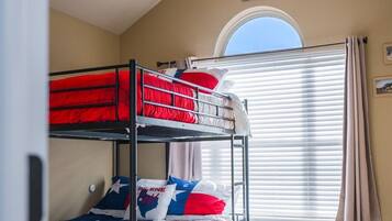 A room with bunk beds, a ceiling fan, a window with blinds, and a rug.