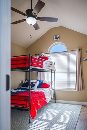 A room with bunk beds, a ceiling fan, a window with blinds, and a rug. - Candy Land Lane- 3 Bedrooms | Retro Game Room! (Abilene)