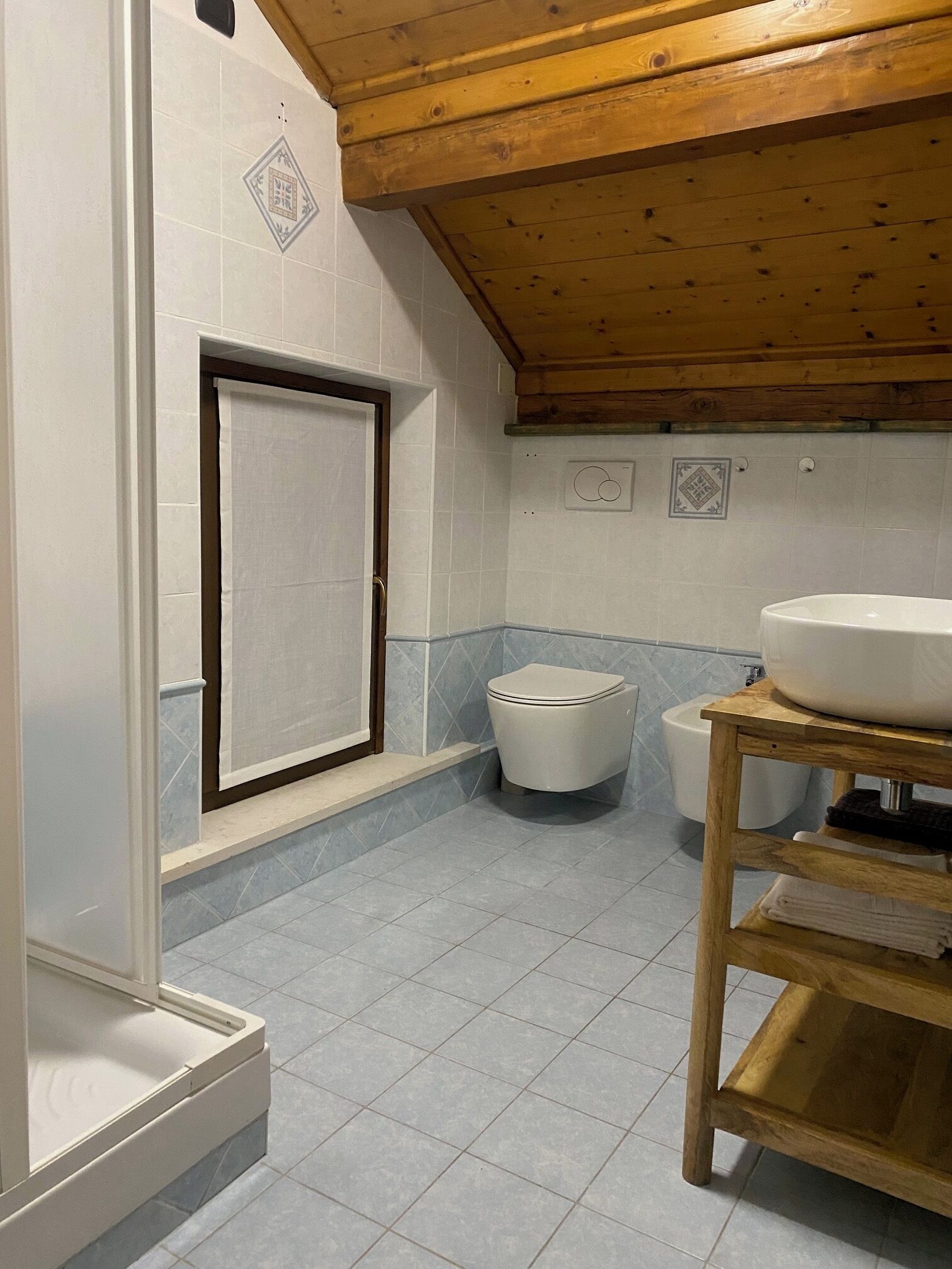 A bathroom with a wooden ceiling, a toilet, a sink on a wooden stand, and a towel rack.