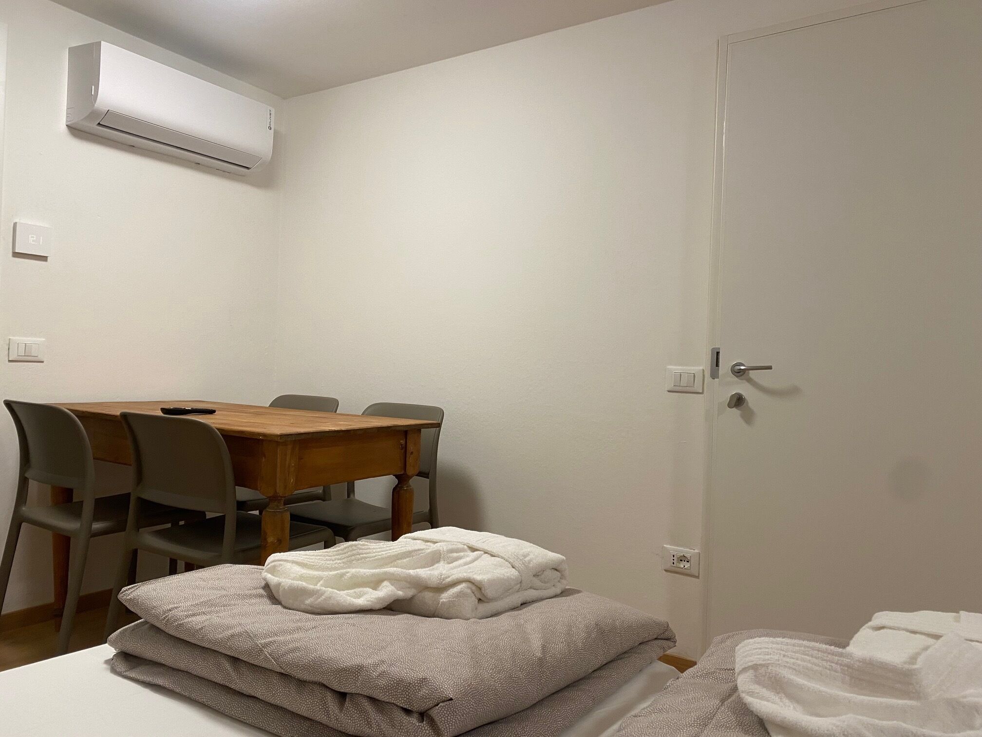 A room with a wooden dining table, four chairs, a white air conditioner, and a door with a handle.