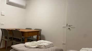 A room with a wooden dining table, four chairs, a white air conditioner, and a door with a handle.