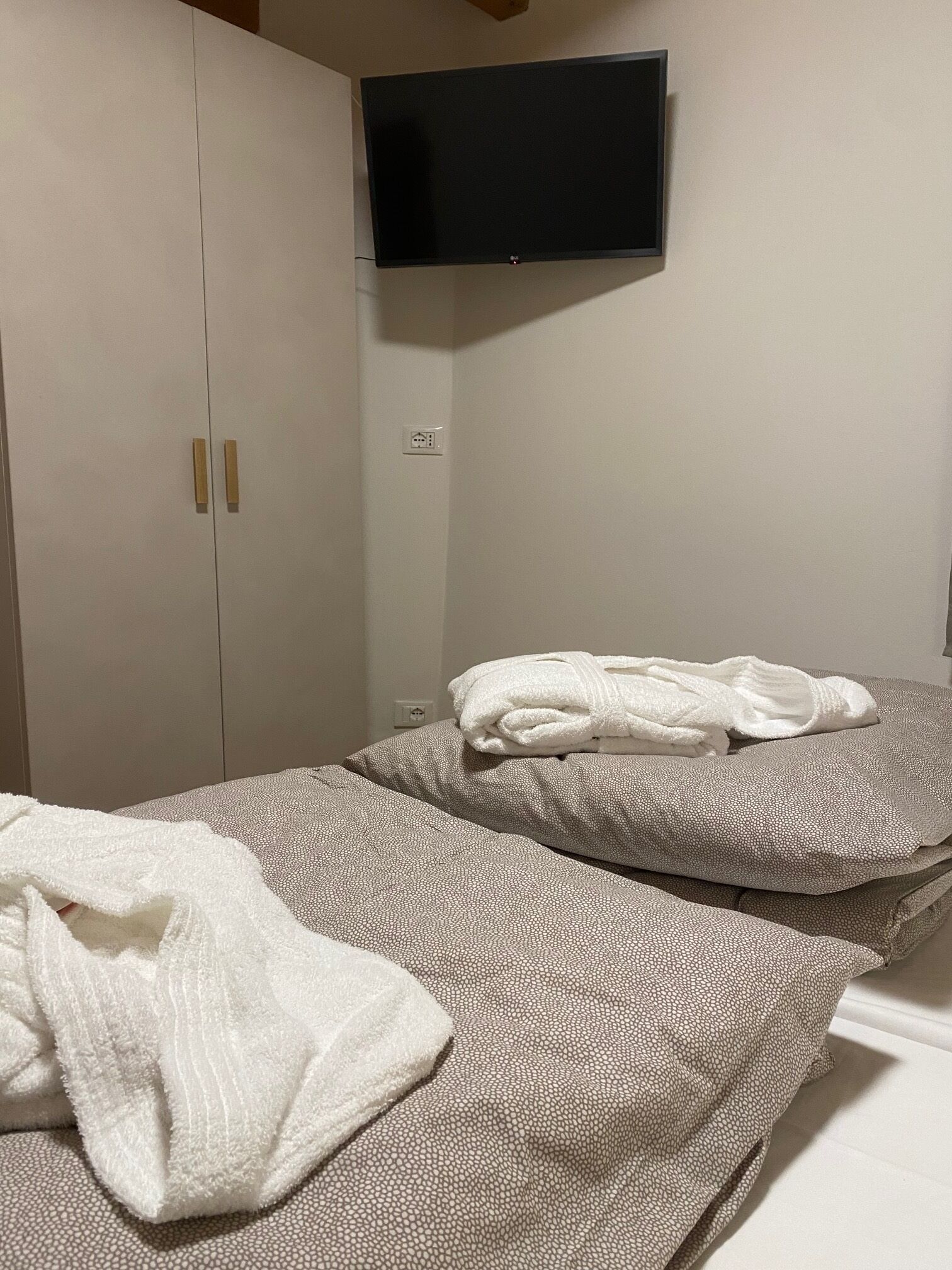 Ein Schlafzimmer mit zwei Betten, einem an der Wand montierten Fernseher und einem Kleiderschrank.